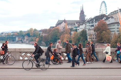 Ca. 20 Menschen aller Altersklassen gehen über die Mittlere Brücke. Im Hintergrund sind der Rhein und die Grossbasler Altstadt mit dem Münster und einem Riesenrad zu sehen.(Copyright Börje Müller)