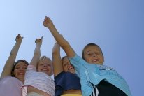 vier Kinder die zusammenstehen und je einen Arm mit dem Daumen nach oben in die Luft strecken